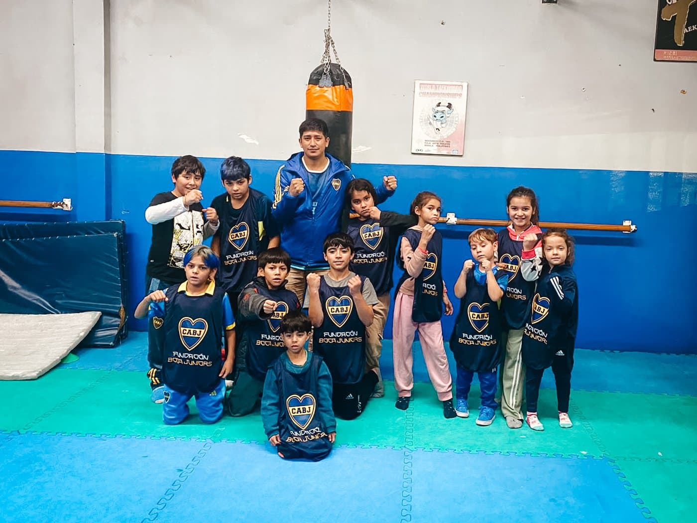Los chicos y chicas de la clínica posan con los puños en guardia junto al profesor, frente a la bolsa de boxeo