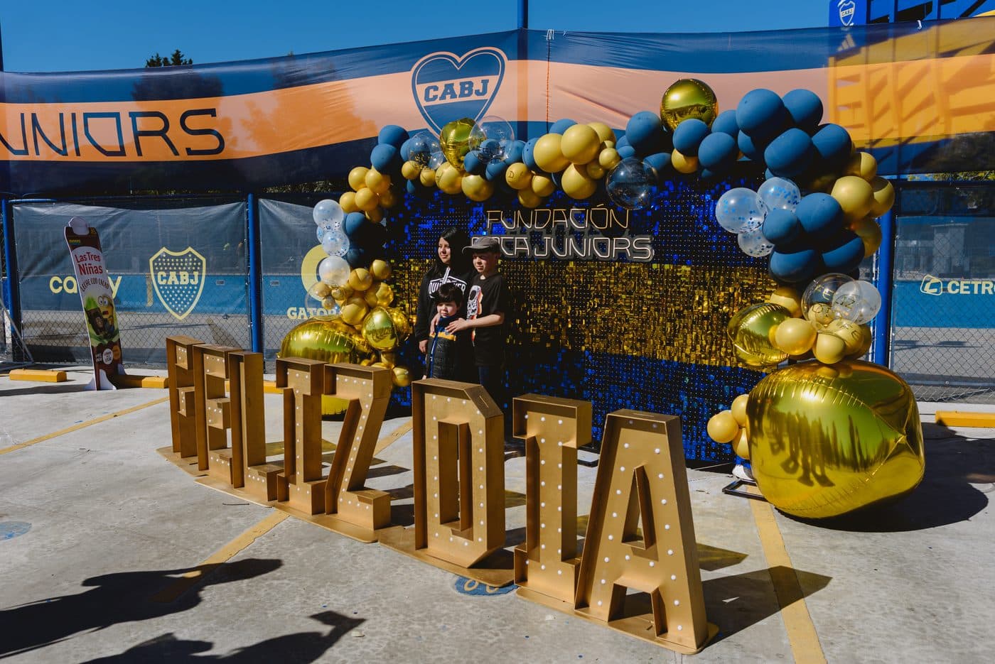 Las letras gigantes de “Feliz día” en dorado, entre globos azules y dorados, frente al muro de la Fundación
