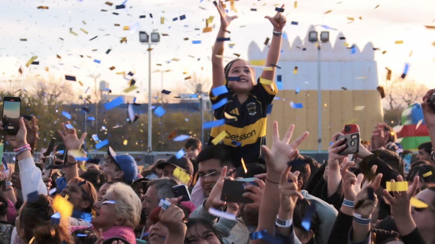 Una chica con la camiseta de Boca alzada en andas, con los brazos en alto entre los papelitos