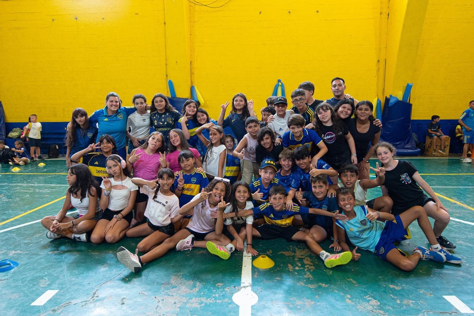 Grupo numeroso de chicos y chicas posando en el piso de un gimnasio durante la colonia de verano