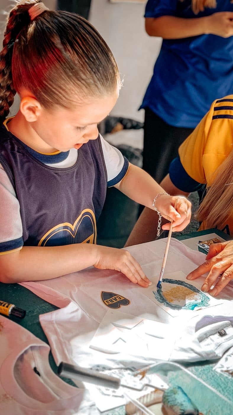 Una nena con la pechera de la Fundación pinta con el dedo el escudo sobre su camiseta