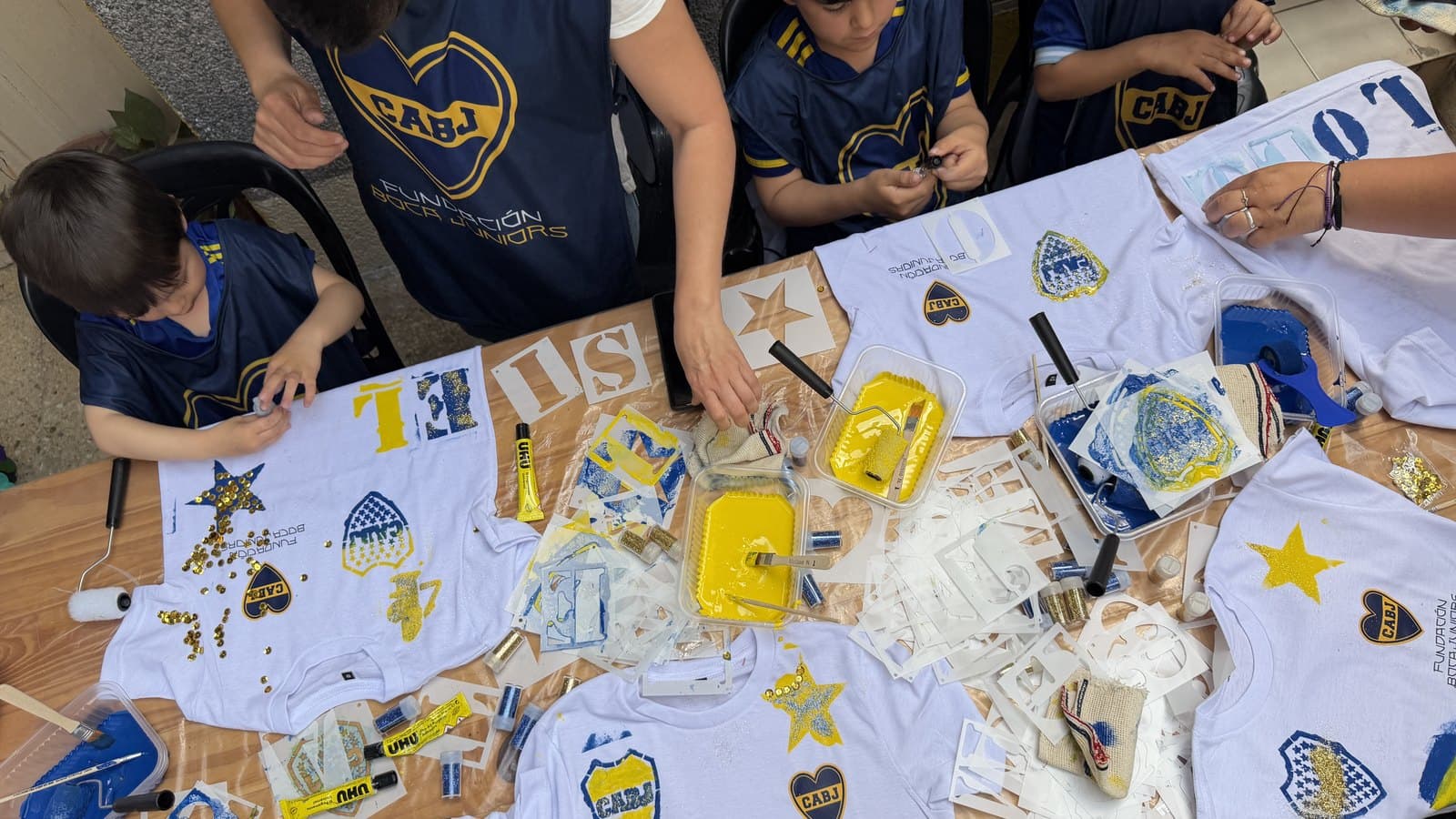 La mesa larga cubierta de camisetas, pinceles y pinturas, con los participantes trabajando alrededor