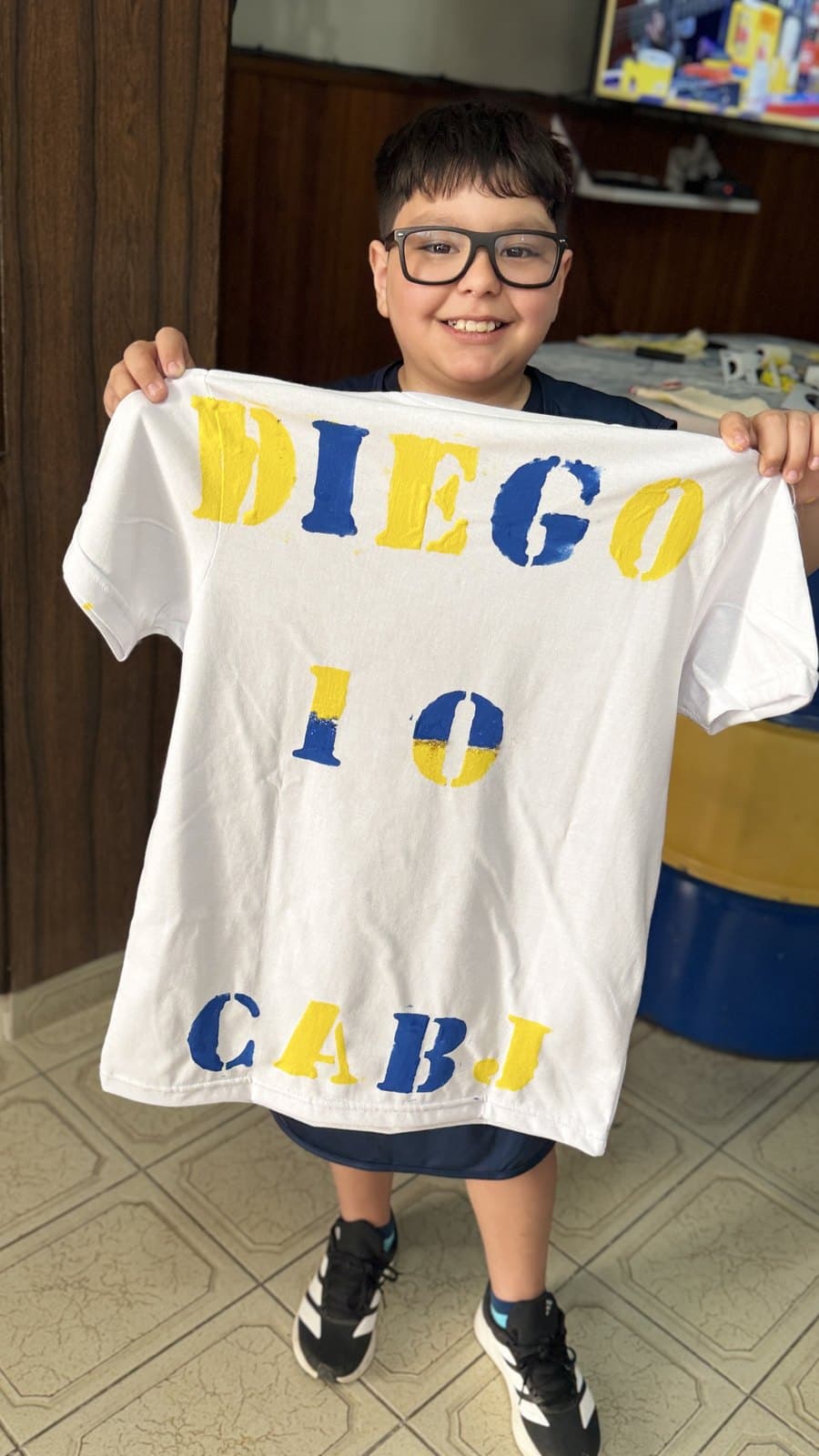 Un nene muestra con las dos manos la camiseta que pintó, con su nombre y el número 10