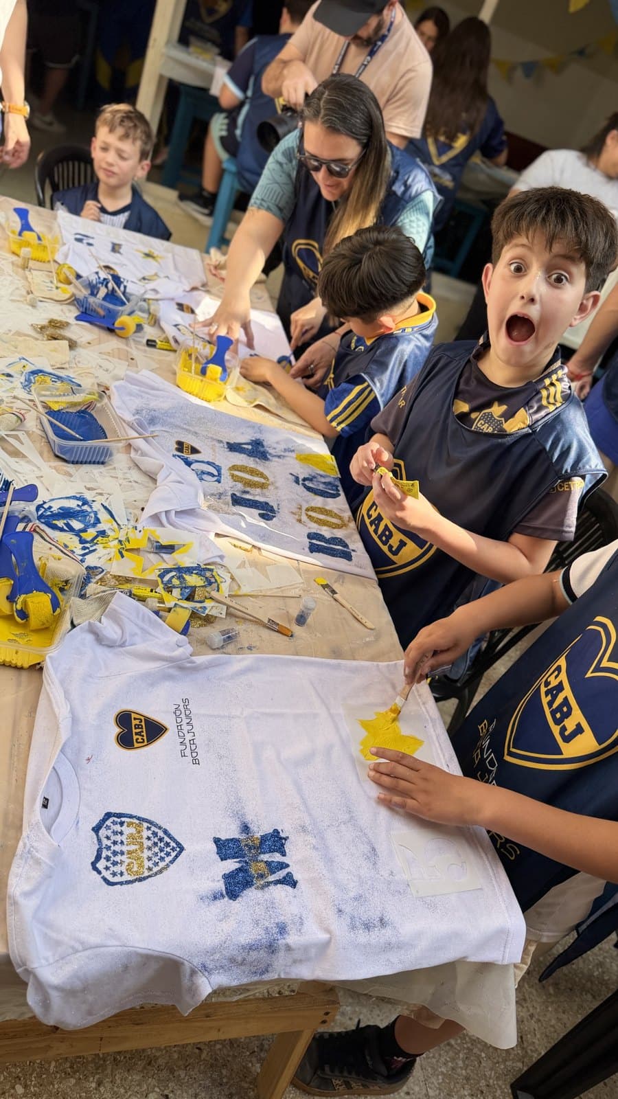 Chicos y chicas con las pecheras de la Fundación pintando sus camisetas sentados a la mesa