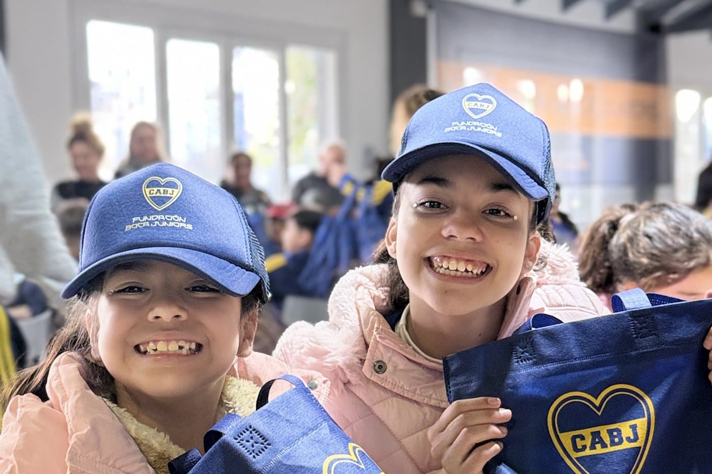 Dos nenas con las gorras de la Fundación sonríen con sus bolsas de regalo sobre la mesa