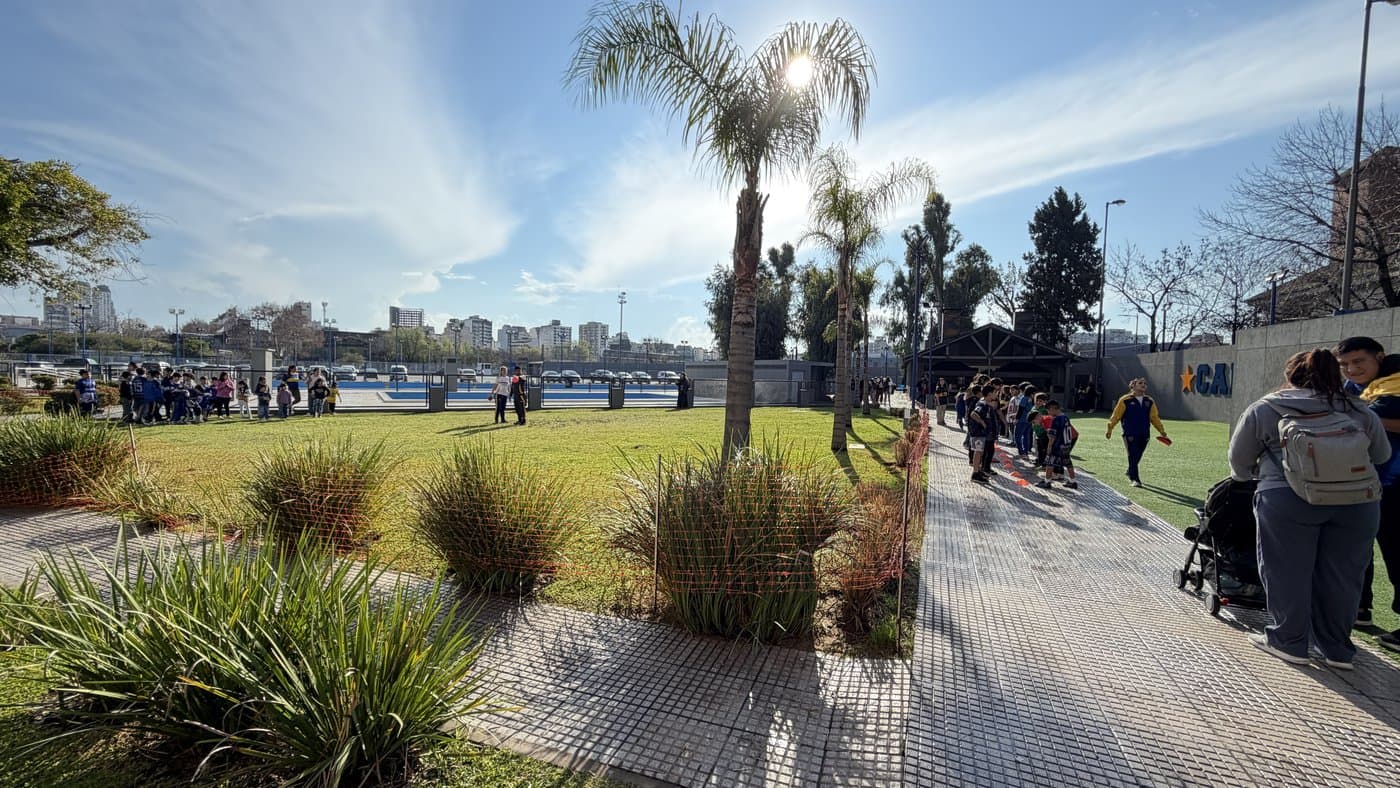 Chicos y familias recorriendo el predio en una mañana de sol, con las canchas al fondo