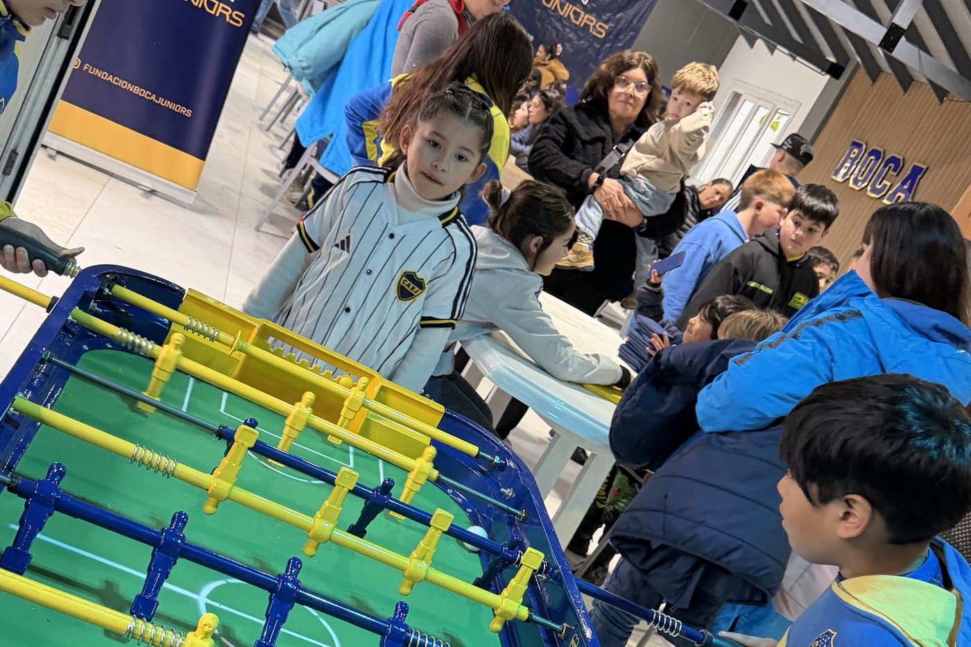 Chicos jugando al metegol en el salón, con los banners de la Fundación de fondo