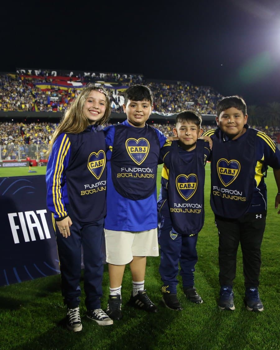 Chicos y chicas con camisetas de la Fundación Boca Juniors en el campo de juego antes de un partido de Copa Argentina