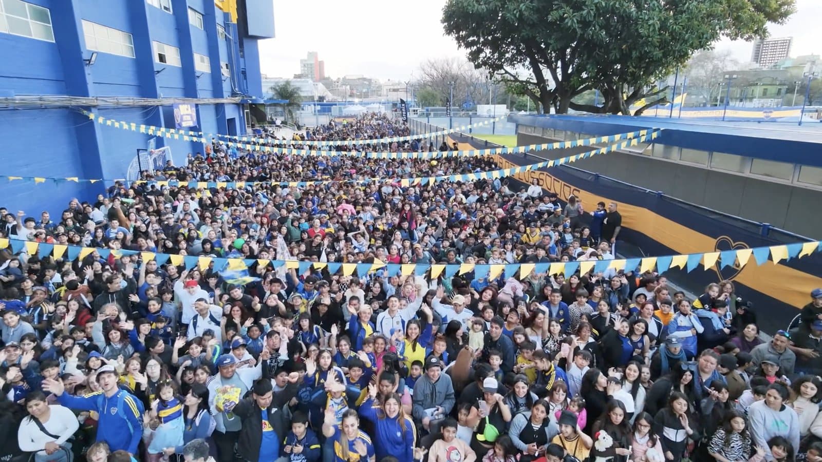 El patio del club repleto de chicos, chicas y familias bajo los banderines azules y blancos