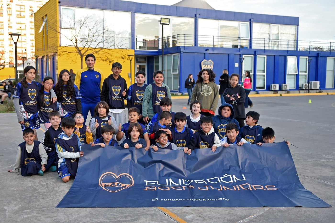 El grupo completo posa con el profesor detrás de la bandera de la Fundación, en la cancha