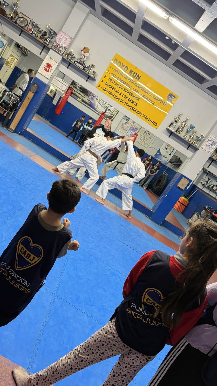 Dos profesores muestran una técnica mientras los chicos miran desde el borde del tatami